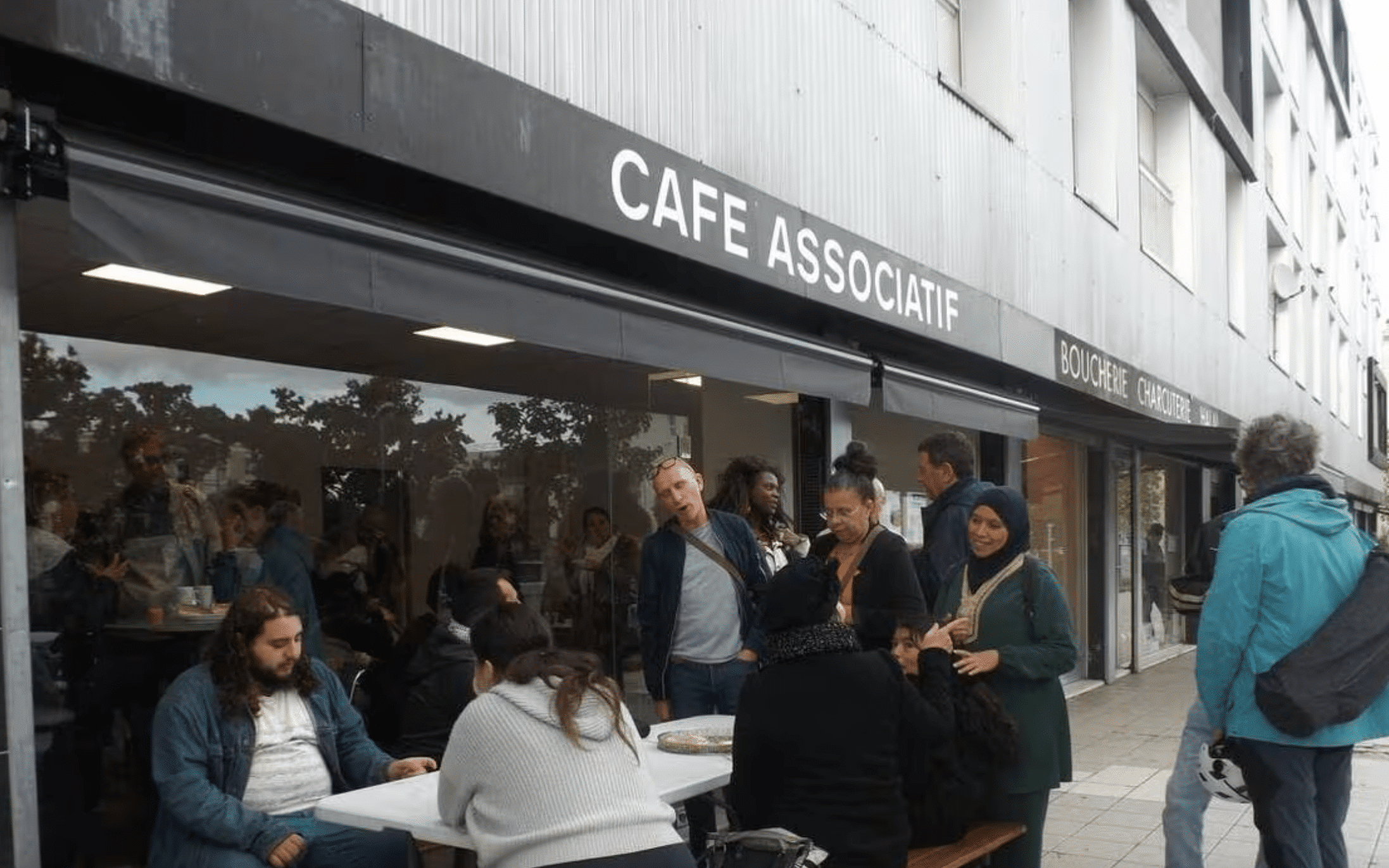 photo de plusieurs personnes devant une facade où il est écrit "café associatif"